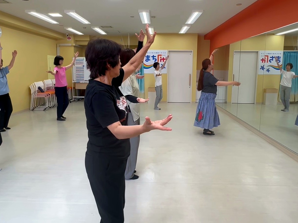 川崎スタジオで、両手を上げてフラを踊る参加者たち